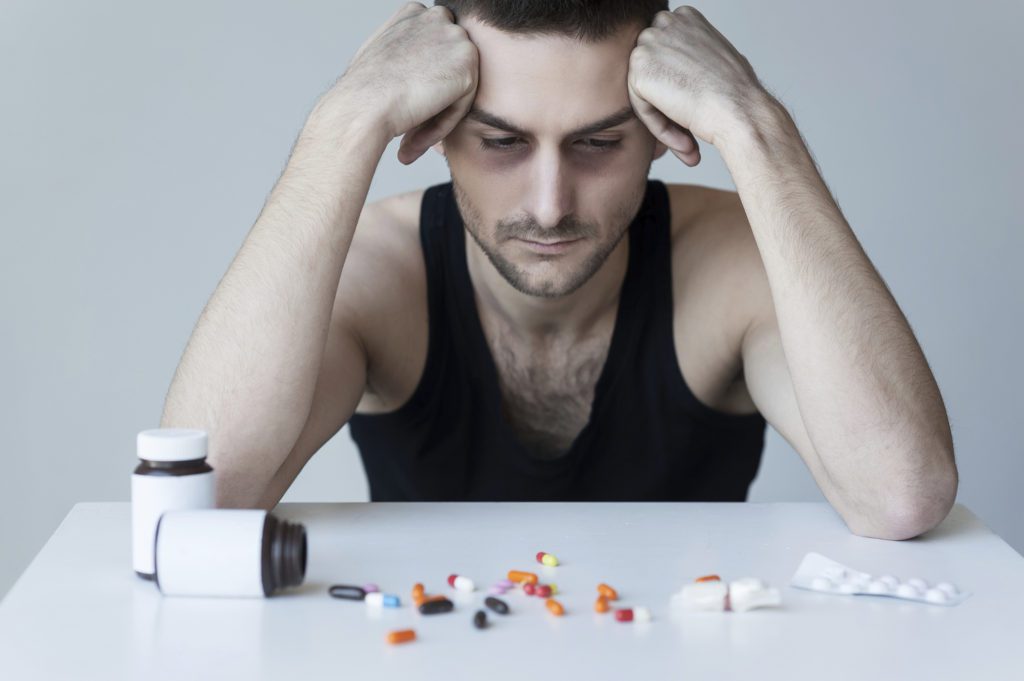 Man looking down regretfully at pills