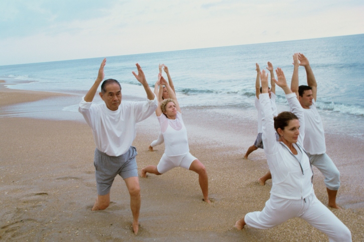 Group of alcoholic patients doing yoga on the beach.