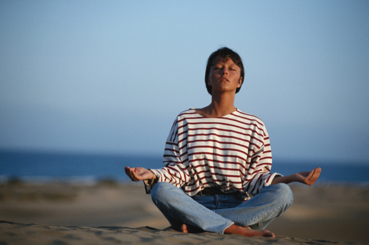 woman meditating while sitting cross legged on beach