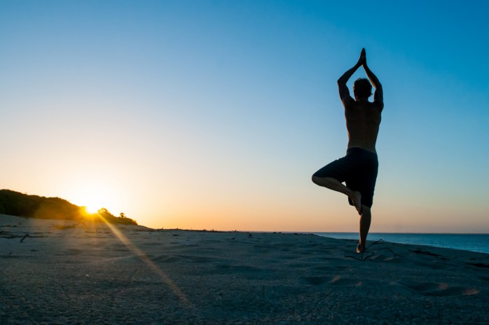 man doing a yoga pose on the beach